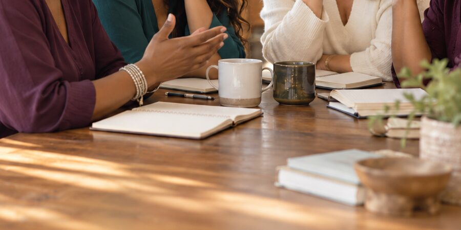 Illustrative detail of hands and notebooks around a discussion table.